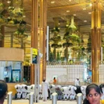 Passengers offering group prayer inside Bengaluru Airport Terminal 2 near the departure area, with airport staff and travellers visible in the background.